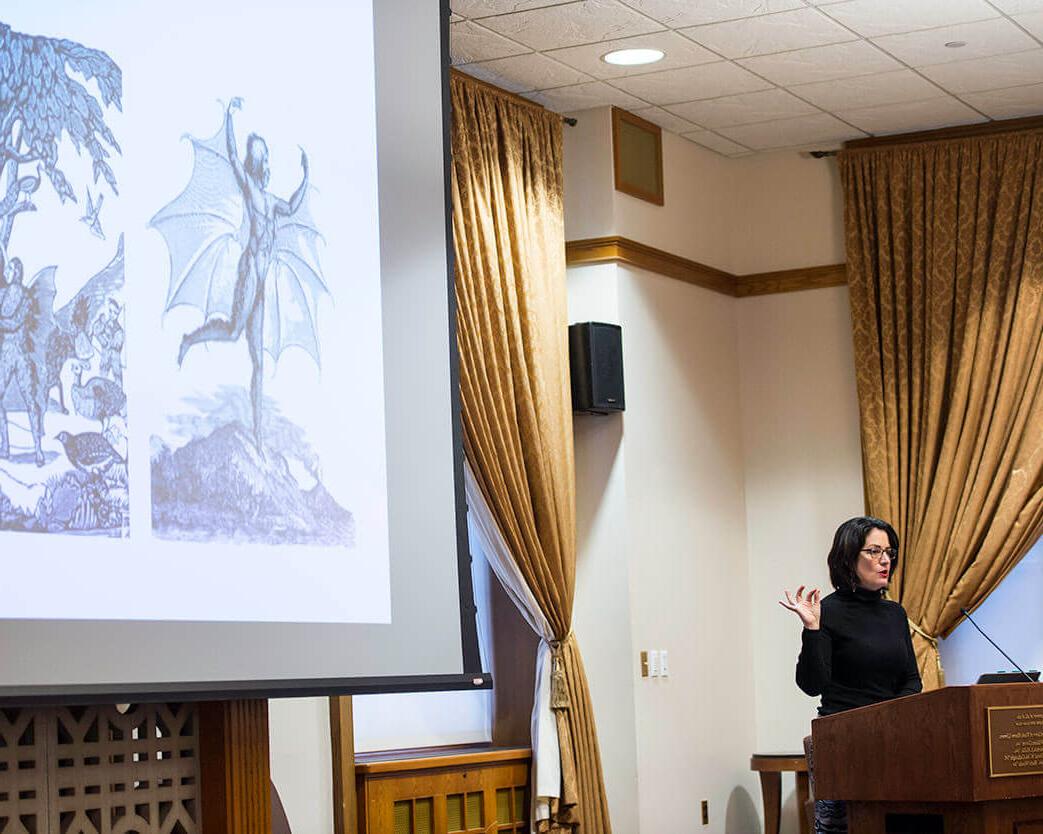 Presenter behind podium in front of projector screen at University of Rochester Humanities Center